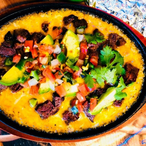 Sizzling skillet of queso fundido with steak, avocado, pico de gallo, and cilantro.