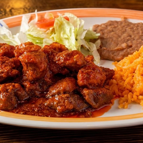 A plate of chili Colorado with rice, refried beans, and a small salad.