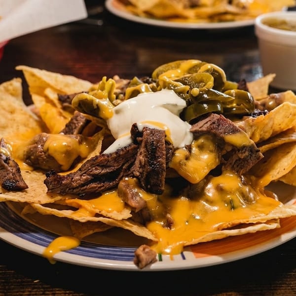 A plate of nachos with steak, melted cheese, sour cream, and jalapeños on a wooden table.
